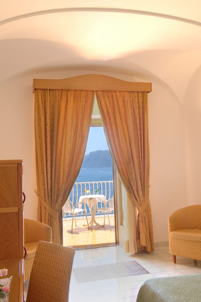 Camera d'albergo luminosa con vista mare da un balcone.