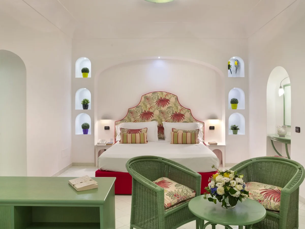 A cozy, elegantly decorated bedroom with white walls, colorful accents, and green wicker furniture.