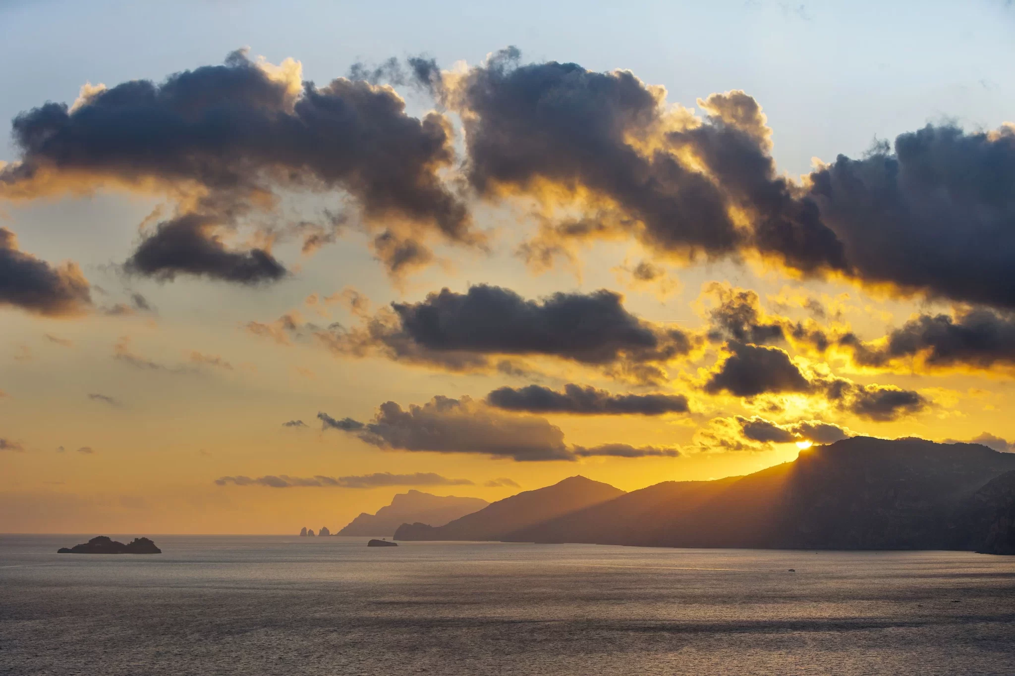 Tramonto nuvoloso sul mare con la silhouette di montagne all'orizzonte.