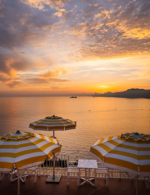 Tramonto suggestivo sul mare con ombrelloni a righe gialle e bianche.