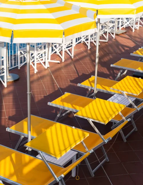 Lettini e ombrelloni a righe gialle e bianche su una terrazza pavimentata.